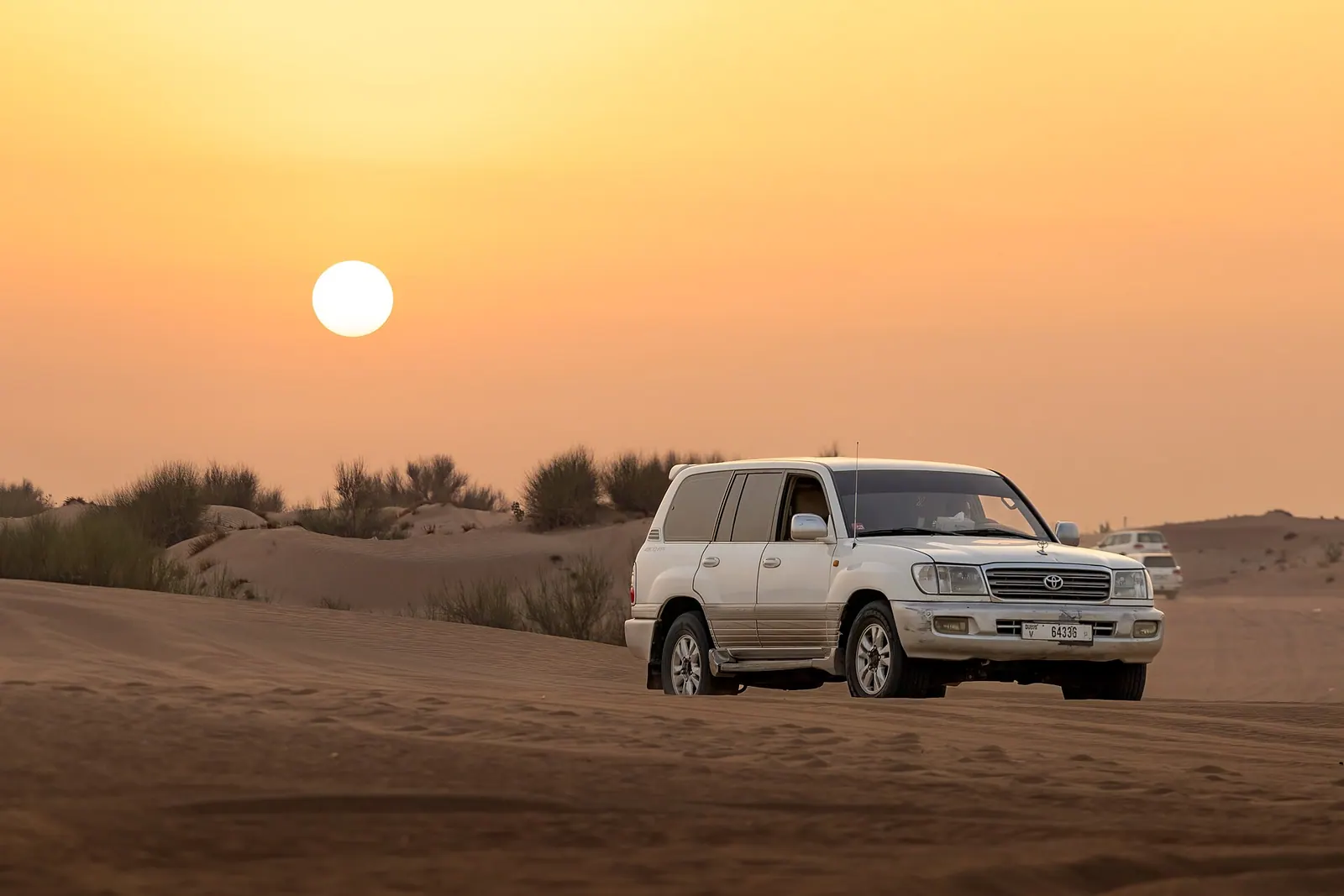4x4 Land Cruiser bashing over red sand dunes at sunset in Dubai desert