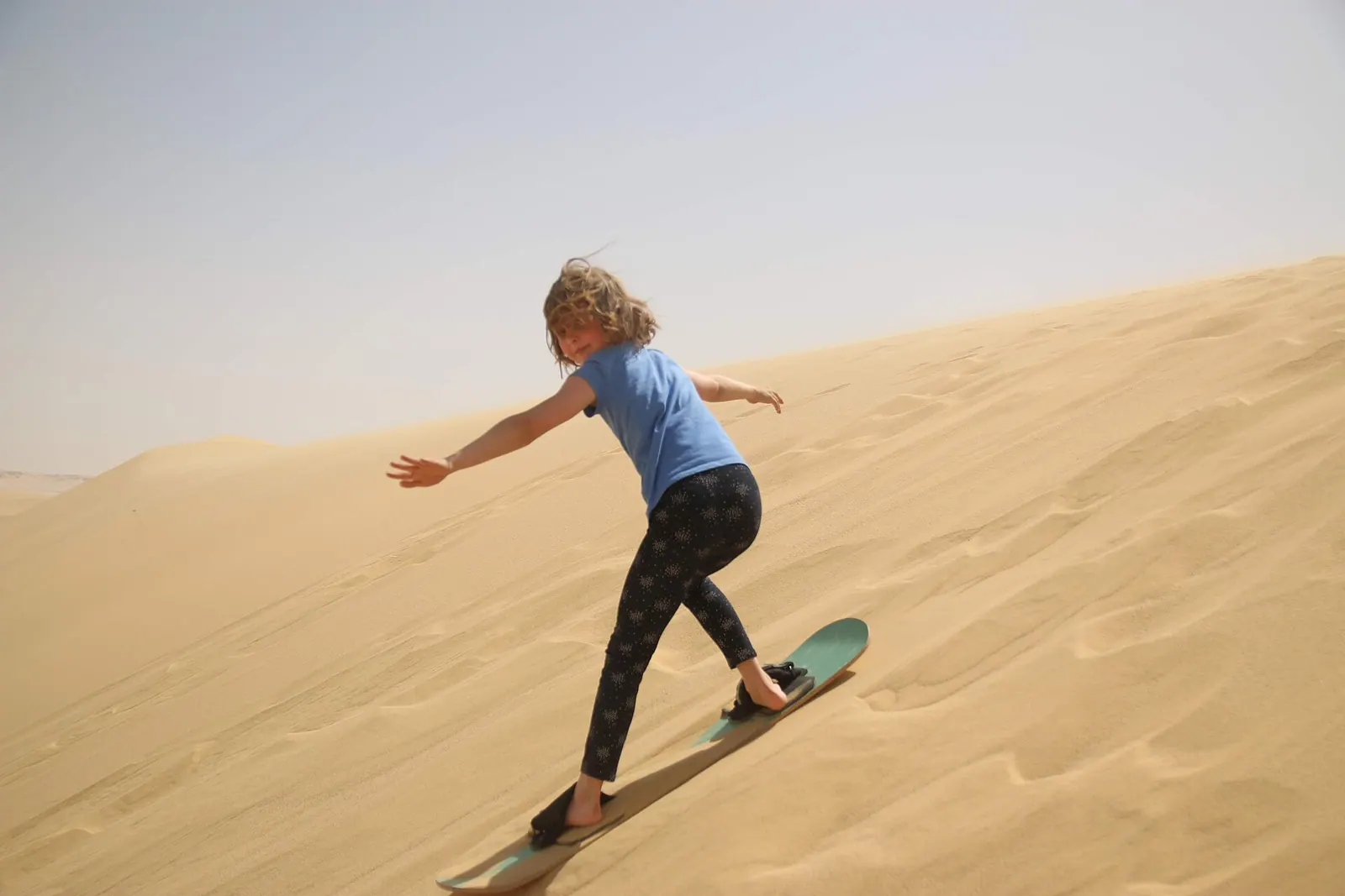 Quad biker speeding down a steep red sand dune in Dubai